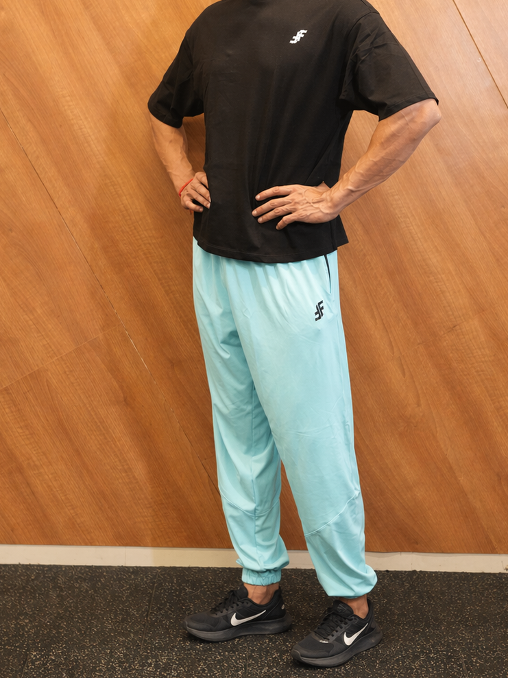 Man wearing a black t-shirt and light blue pants with a brand logo against a wooden wall.